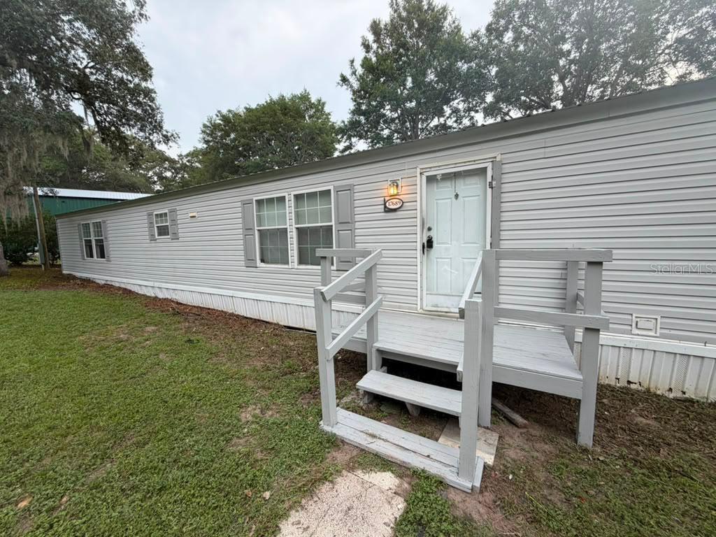 A light gray mobile home exterior features a wooden porch with stairs and white siding — 17689 SE 14TH STREET, SILVER SPRINGS, FL
