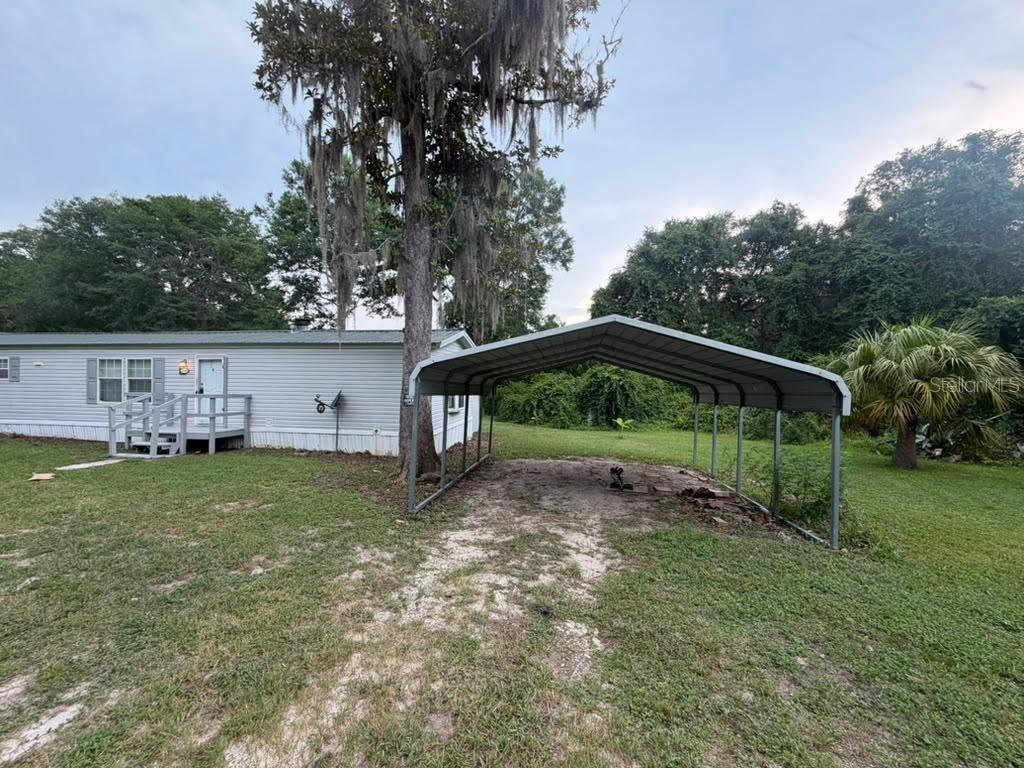A mobile home with a wooden deck and a metal carport in a grassy yard — 17689 SE 14TH STREET, SILVER SPRINGS, FL