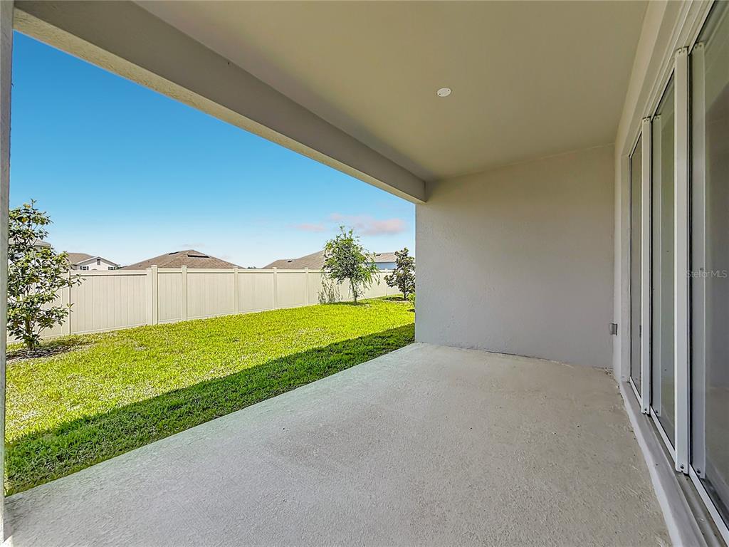 A covered concrete patio overlooks a fenced backyard with a lawn and young trees — 4485 DAVOS DRIVE, CLERMONT, FL