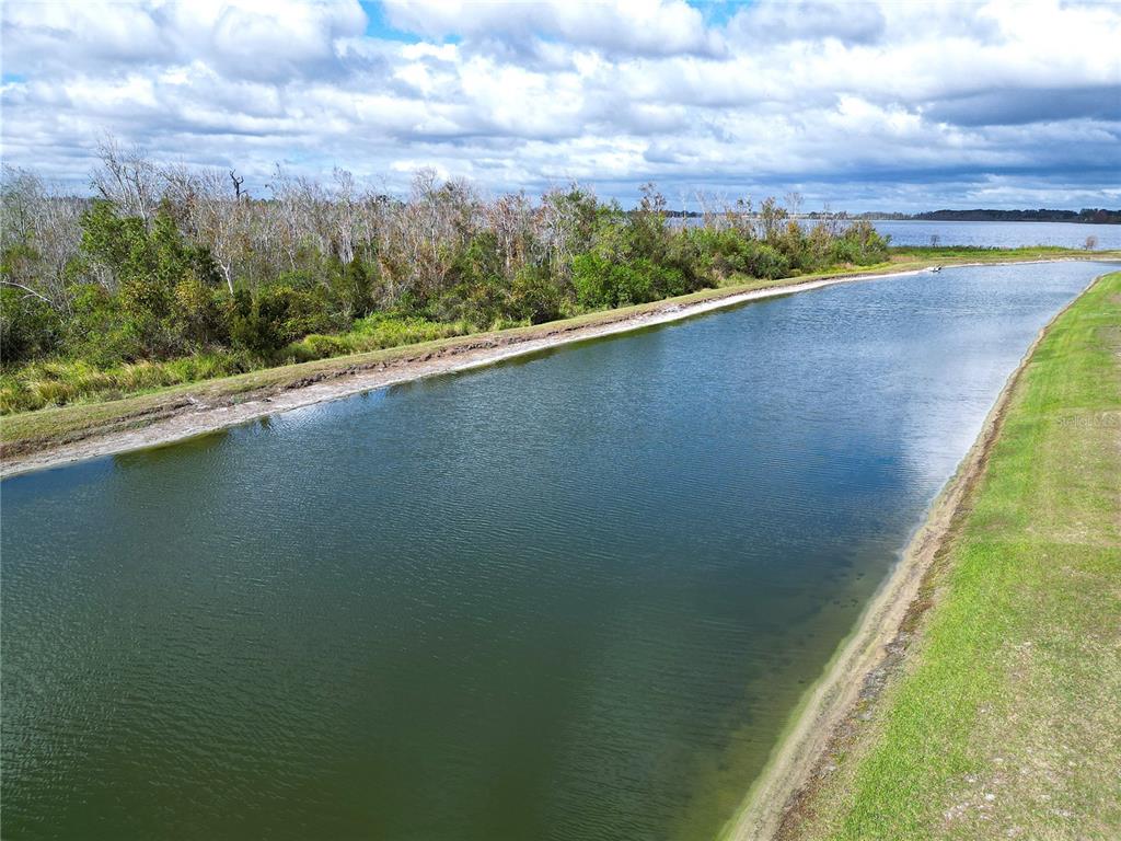 A long, narrow canal runs alongside a grassy bank toward a larger body of water — 465 ADAMS VIEW LANE, AUBURNDALE, FL