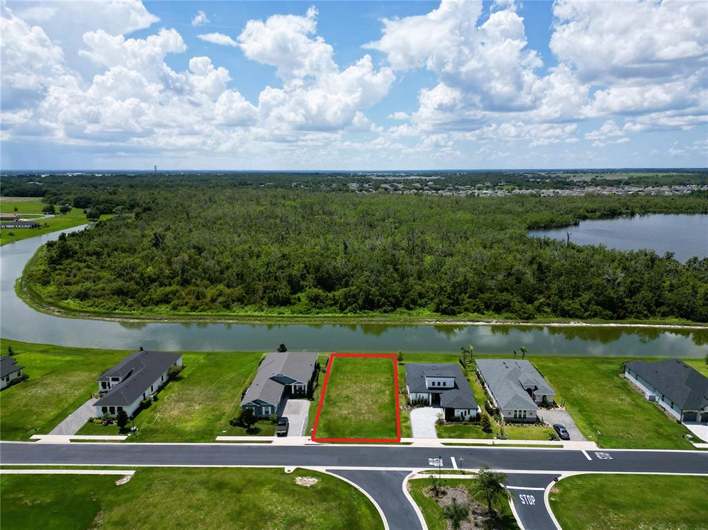 An aerial view shows a vacant rectangular residential lot situated between two houses near water — 465 ADAMS VIEW LANE, AUBURNDALE, FL