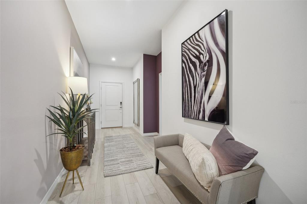 A bright entryway features light wood-look flooring, a zebra print wall art, and a small bench — 9241 HARRIS HAWK DRIVE, LEESBURG, FL
