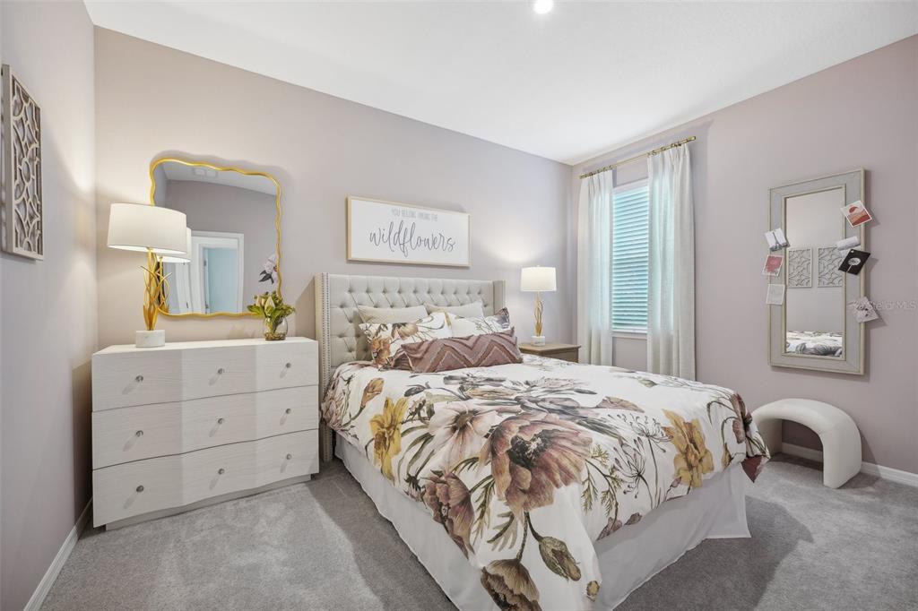 A bedroom features a tufted headboard, floral bedding, a white dresser, and two wall mirrors — 9241 HARRIS HAWK DRIVE, LEESBURG, FL