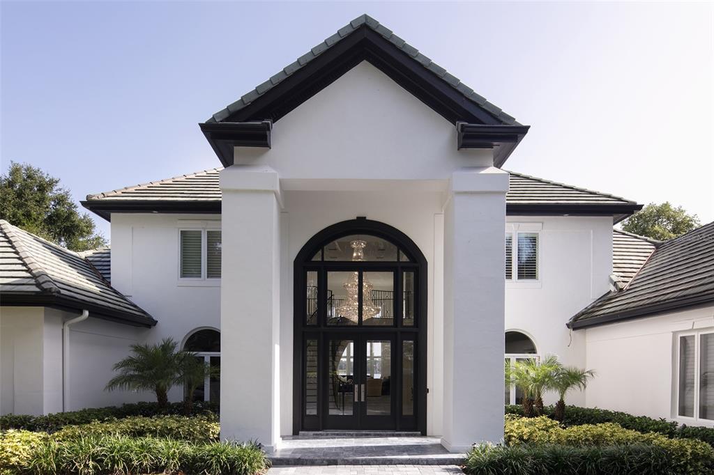 The exterior of a white house features a prominent arched entryway with a large chandelier — 6462 DEACON CIR, WINDERMERE, FL