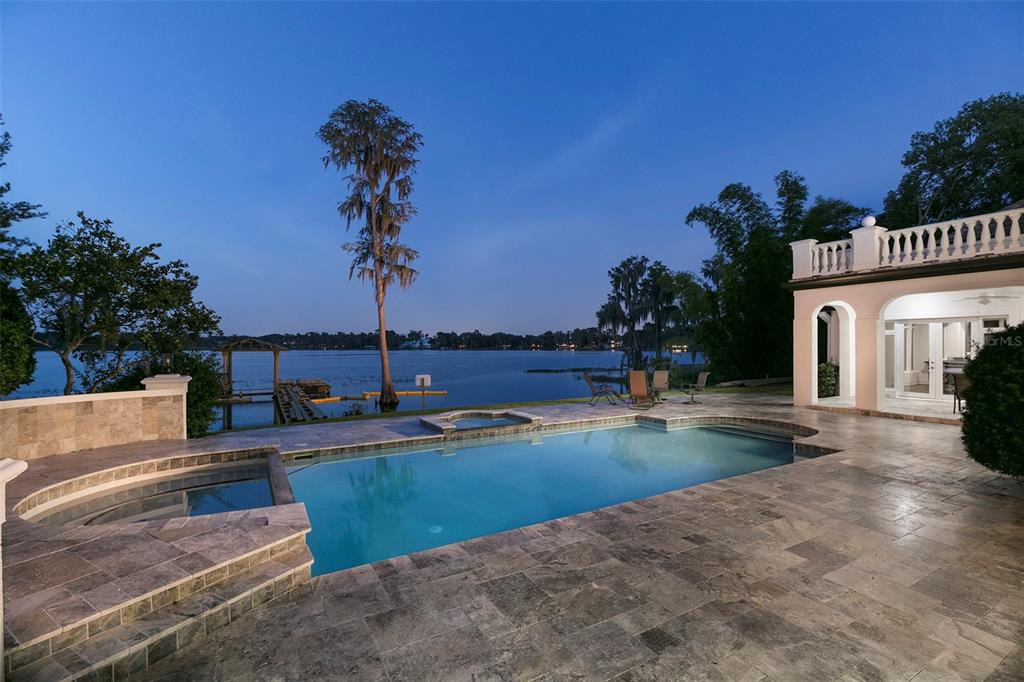 A swimming pool and spa sit on a stone patio overlooking a lake at dusk — 6462 DEACON CIR, WINDERMERE, FL