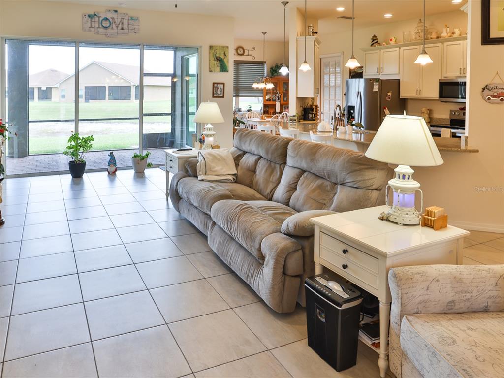 A living room with tile floors, a beige sofa, and a view of the backyard — 1061 SAWGRASS DRIVE, WINTER HAVEN, FL