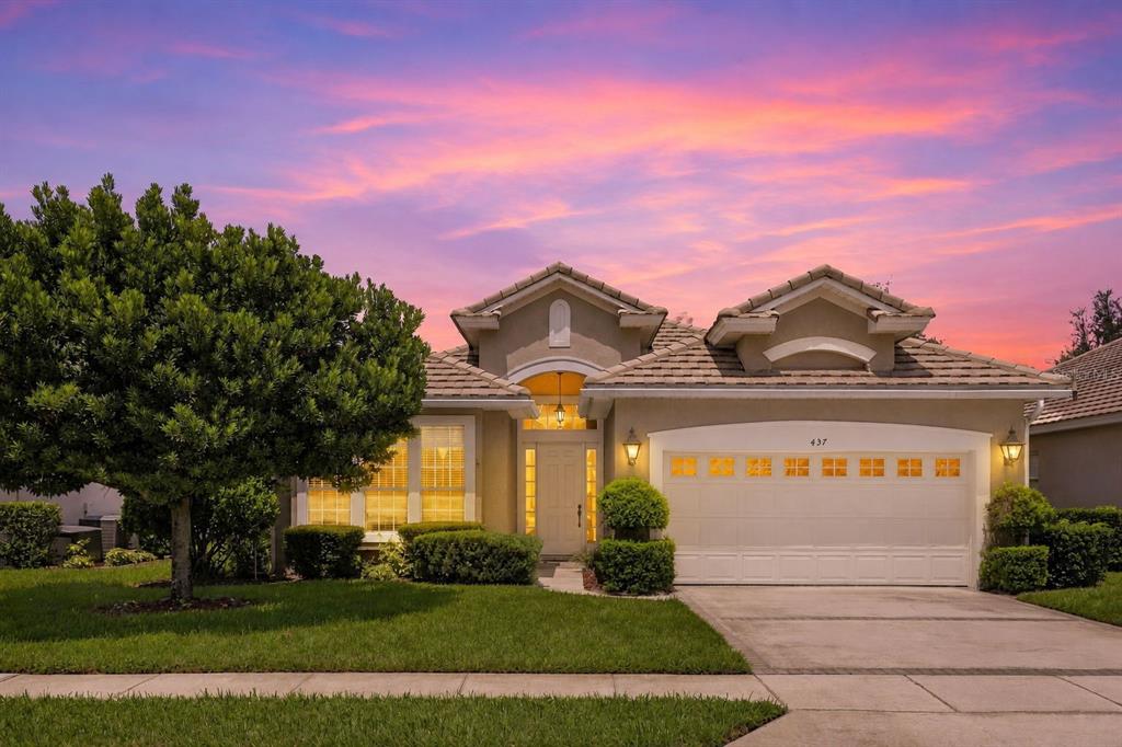 A single-story suburban house with a tan stucco exterior, a two-car garage, and a sunset sky — 437 SOTHEBY WAY, DEBARY, FL