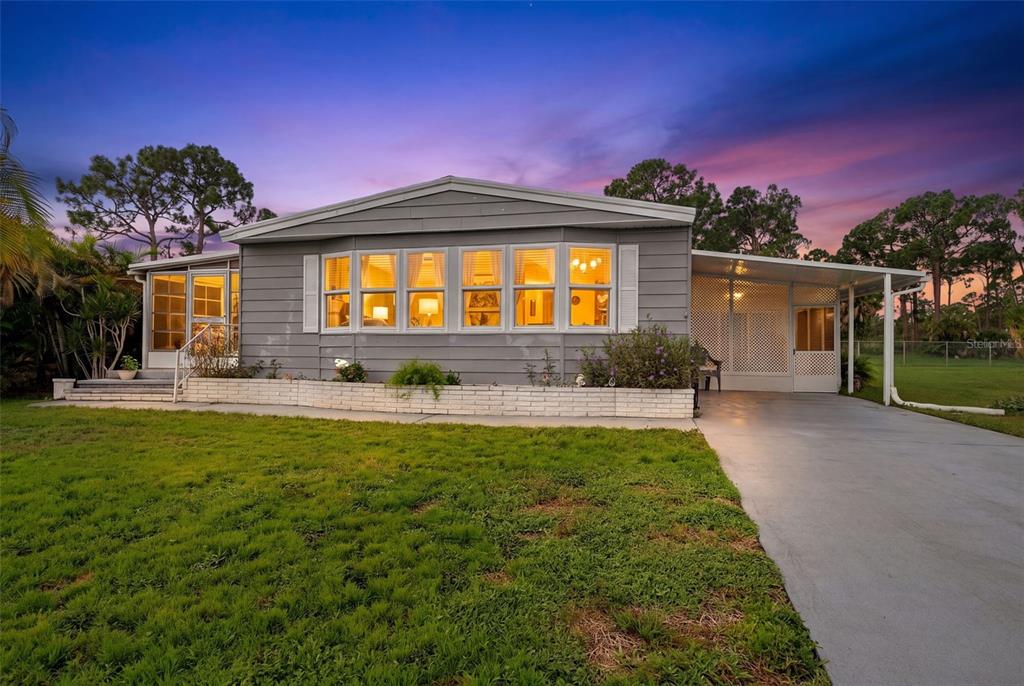 A gray single-story house with a white brick planter and a concrete driveway at sunset — 417 VILLA NUEVA CIRCLE, NORTH PORT, FL