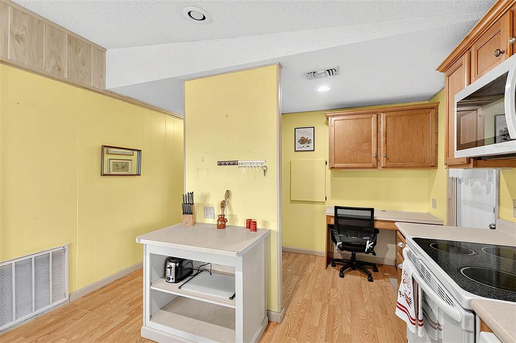 A kitchen with yellow walls, wood cabinets, a small island, and a built-in desk area — 417 VILLA NUEVA CIRCLE, NORTH PORT, FL