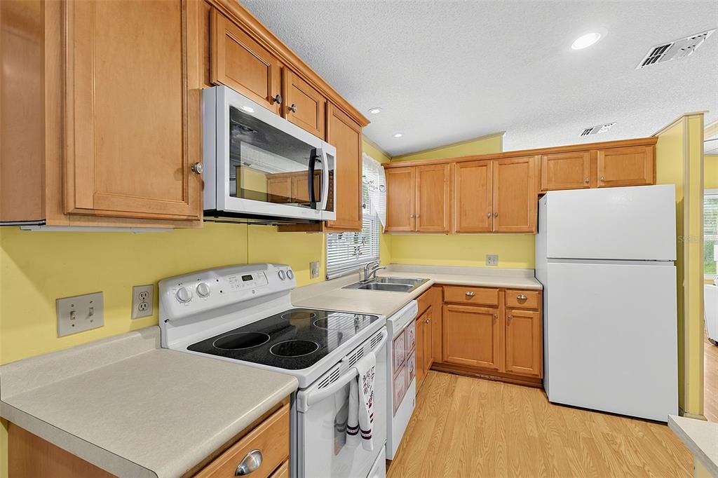 A kitchen with light wood cabinets, yellow walls, white appliances, and light-colored laminate countertops — 417 VILLA NUEVA CIRCLE, NORTH PORT, FL