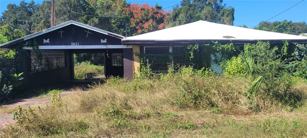A single-story house with a carport and overgrown yard is shown under a clear sky — 5451 LILY ROAD, LAKELAND, FL