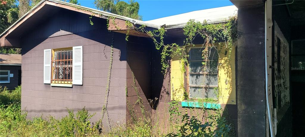 The exterior of a small, weathered house features dark siding, overgrown vines, and barred windows — 5451 LILY ROAD, LAKELAND, FL