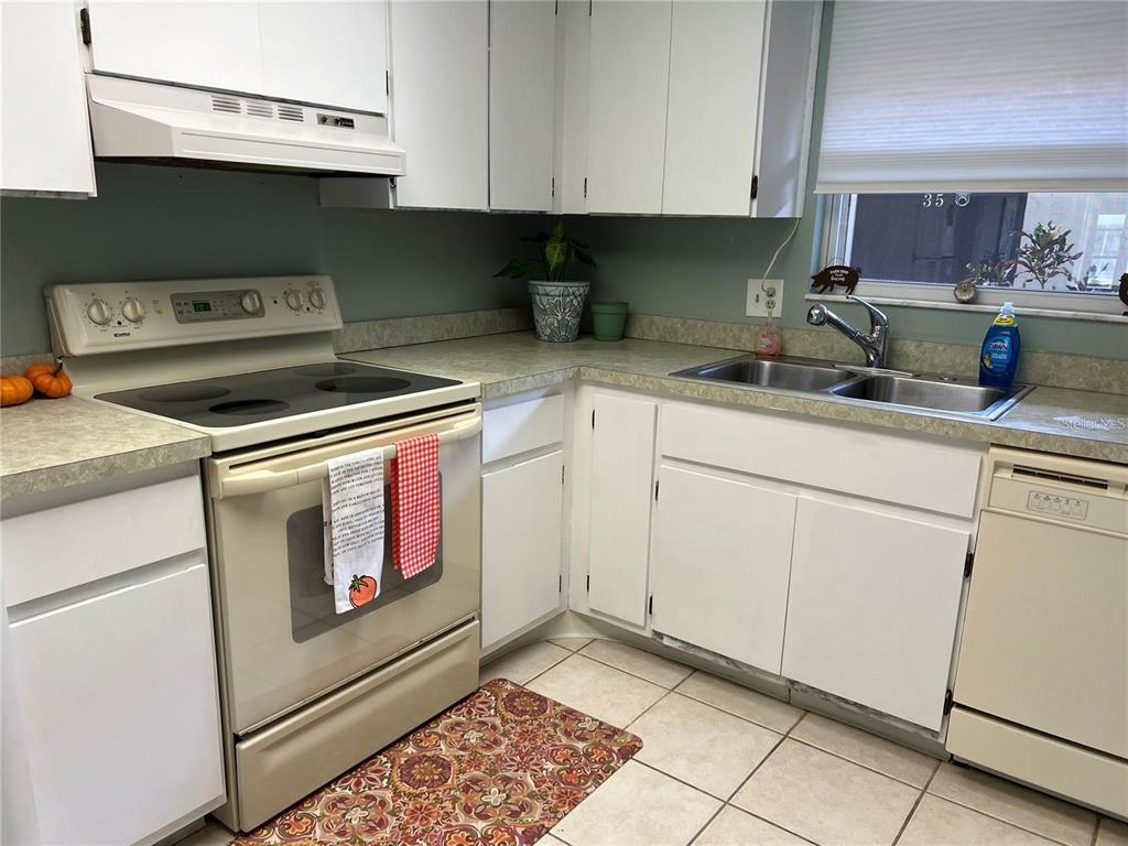 A kitchen features white cabinets, a light-colored countertop, a stove, and a double sink — 1100 E BAY DRIVE UNIT 35, LARGO, FL