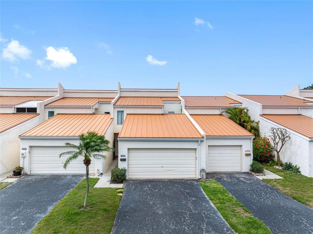 A row of townhouses features metal roofs, white stucco walls, and individual garage doors — 4306 SUNRAY COURT, TAMPA, FL