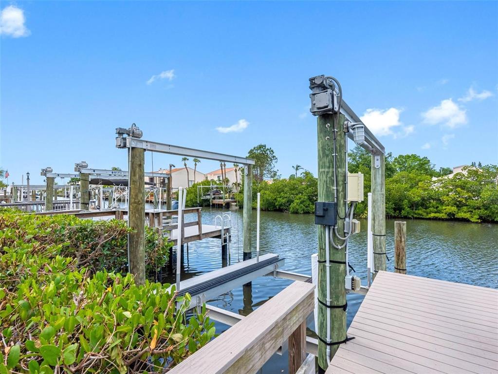 A boat lift stands above a canal next to a wooden dock and green foliage — 4306 SUNRAY COURT, TAMPA, FL