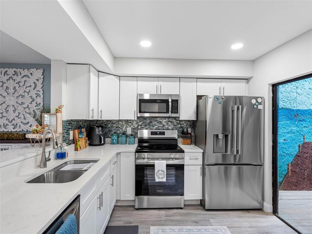 A kitchen features white cabinets, stainless steel appliances, quartz countertops, and a glass tile backsplash — 4306 SUNRAY COURT, TAMPA, FL