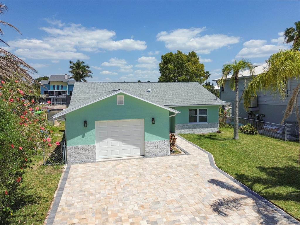 A light green house with a stone-accented base, a white garage door, and a paver driveway — 4482 KINGSTON DRIVE, HERNANDO BEACH, FL