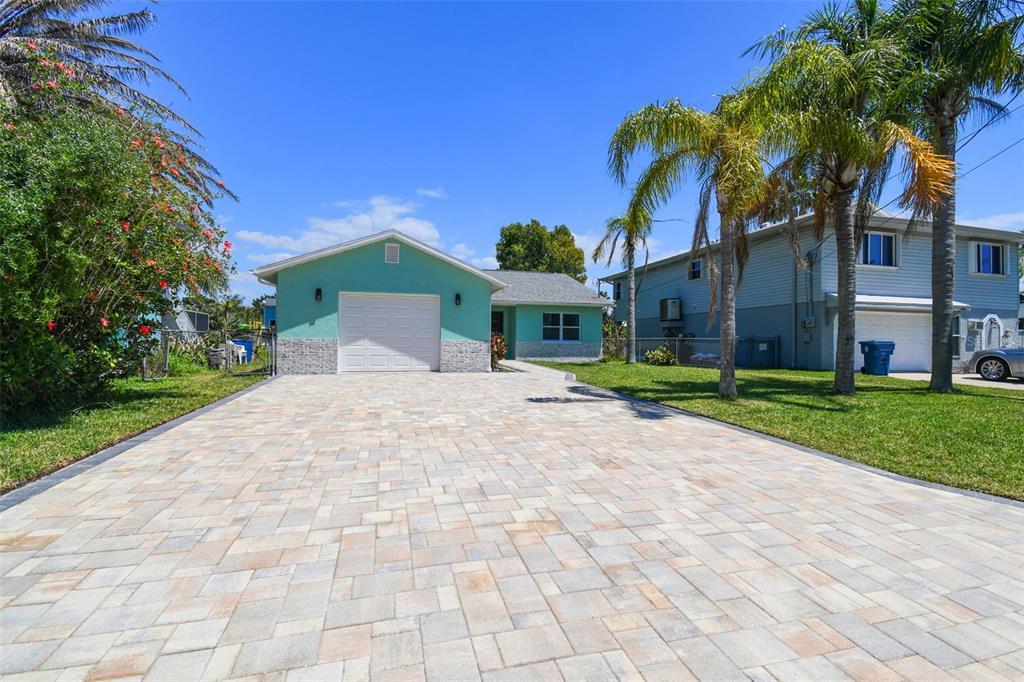A teal house with a stone-accented garage and a large paver driveway under a blue sky — 4482 KINGSTON DRIVE, HERNANDO BEACH, FL