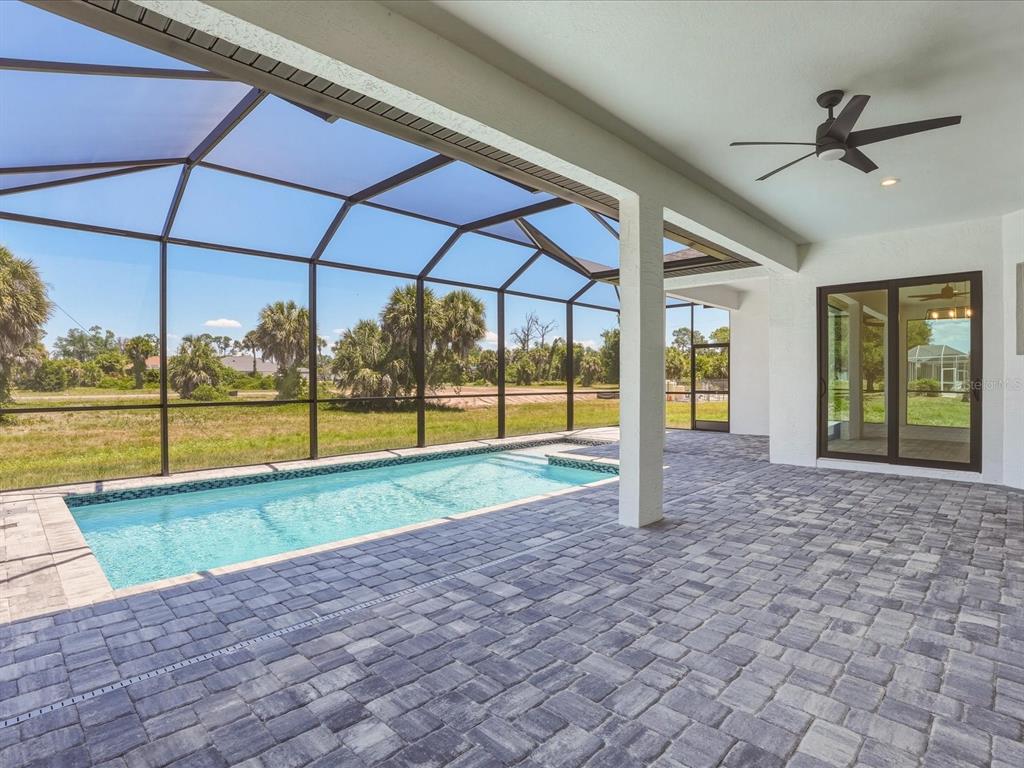 A covered patio with a pool and screen enclosure overlooks an open grassy field — 72 TEE VIEW ROAD, ROTONDA WEST, FL