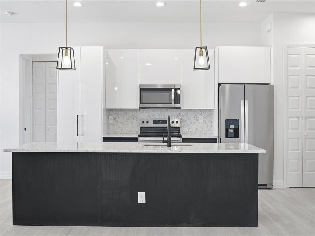 A modern kitchen features a black island, white cabinets, stainless steel appliances, and marble countertops — 72 TEE VIEW ROAD, ROTONDA WEST, FL