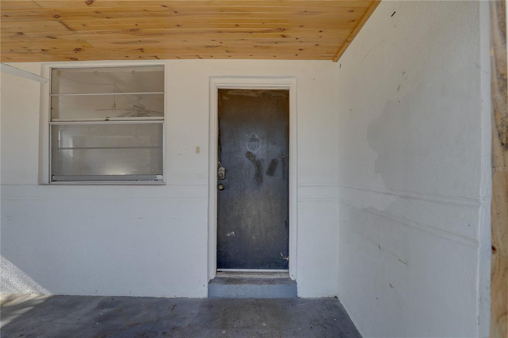 A covered porch features a dark metal door, a window, and a wood-paneled ceiling — 440 S BAYSHORE DRIVE, MADEIRA BEACH, FL