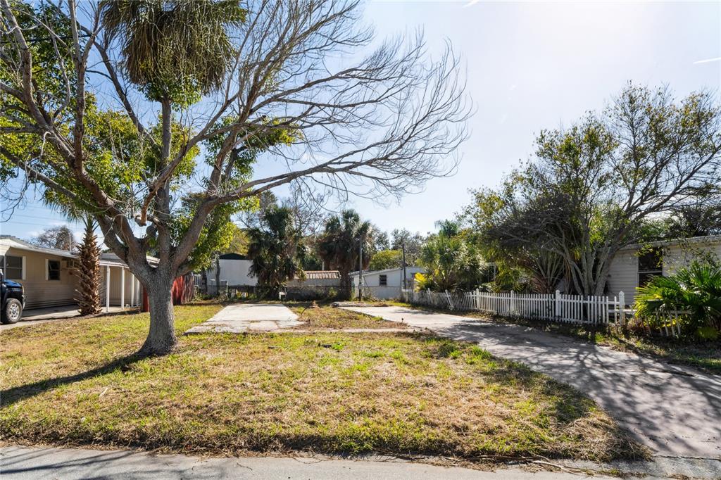 A concrete driveway leads toward a mobile home with a red fence and surrounding trees — 736 DRIFTWOOD LANE, TARPON SPRINGS, FL