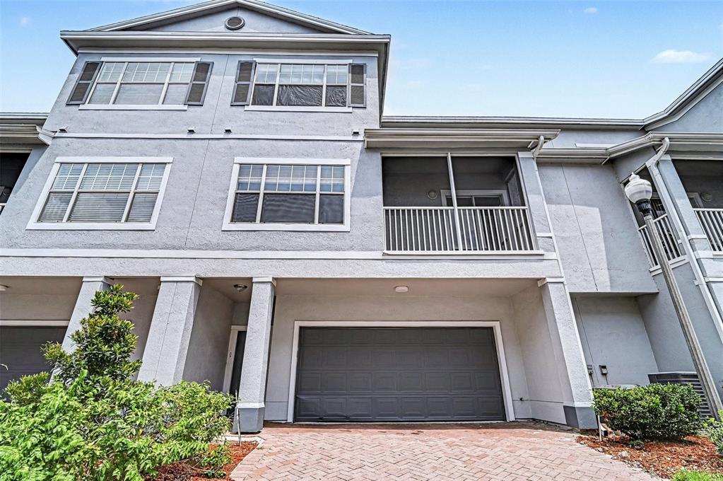 A three-story townhouse exterior features a gray stucco facade, a garage, and a screened balcony — 2460 GRAND CENTRAL PARKWAY UNIT 9, ORLANDO, FL