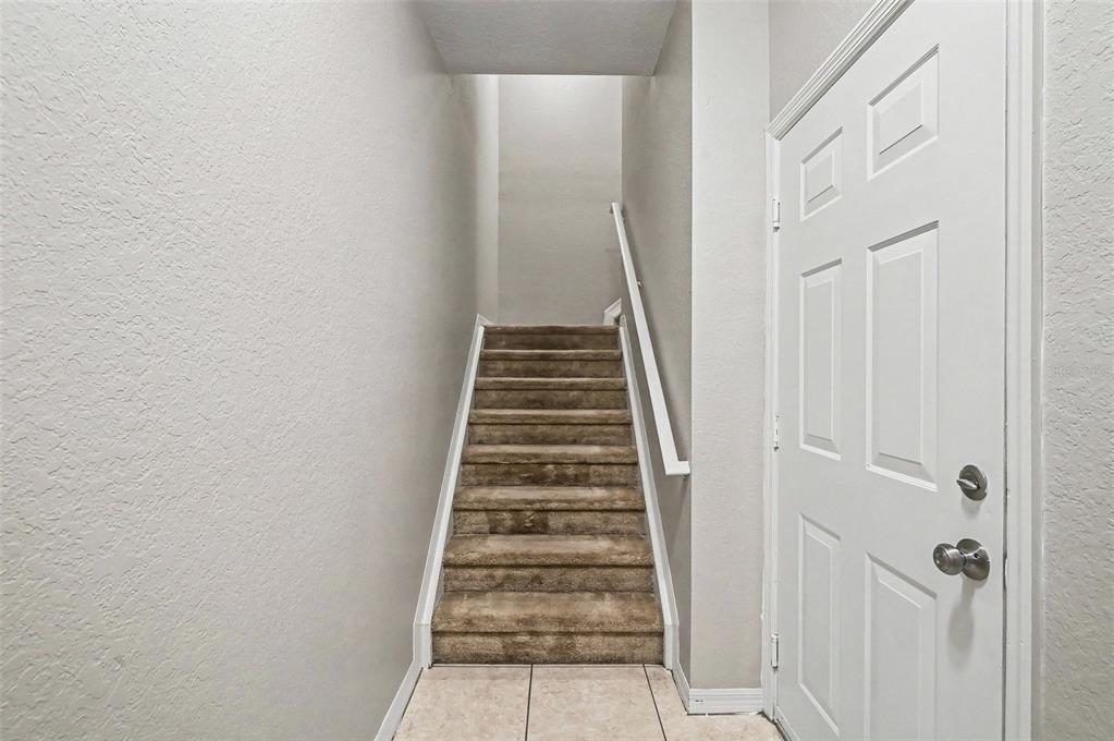 A carpeted staircase leads upward between a plain wall and a white entry door — 2460 GRAND CENTRAL PARKWAY UNIT 9, ORLANDO, FL
