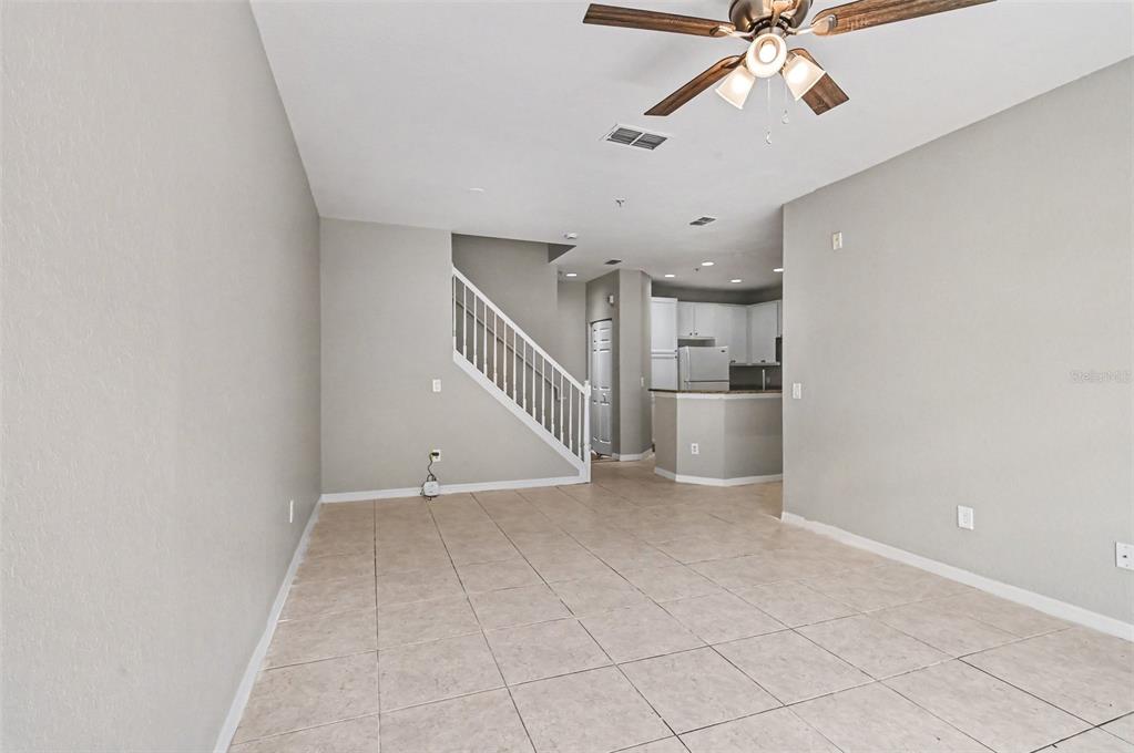 An open-concept living area features tile flooring, a white staircase, and a kitchen beyond — 2460 GRAND CENTRAL PARKWAY UNIT 9, ORLANDO, FL
