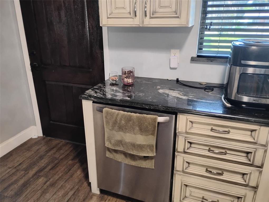 A kitchen features a stainless steel dishwasher, dark granite countertops, and light-colored cabinetry — 2101 N ATLANTIC AVENUE UNIT 18, DAYTONA BEACH, FL