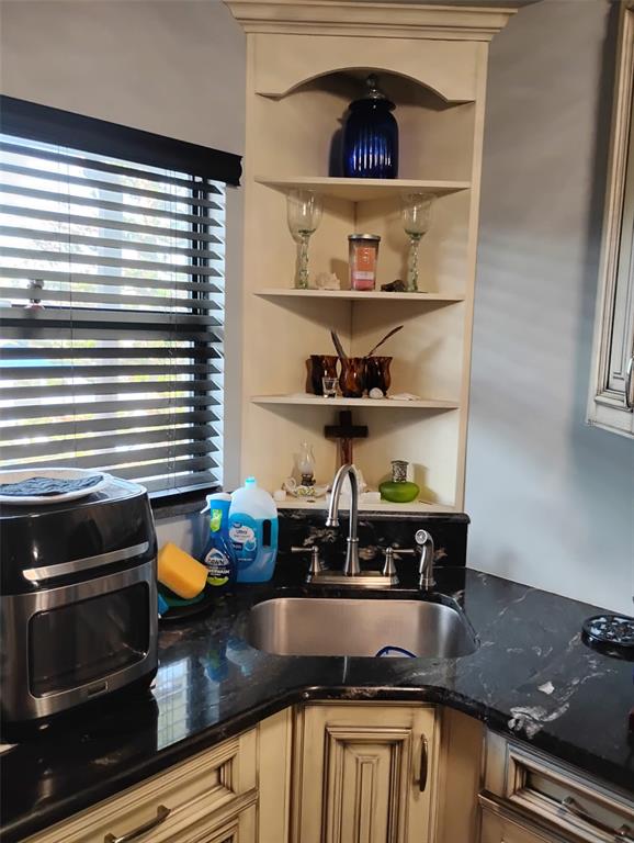 A corner kitchen sink features dark granite countertops, cream-colored cabinetry, and open shelving above — 2101 N ATLANTIC AVENUE UNIT 18, DAYTONA BEACH, FL