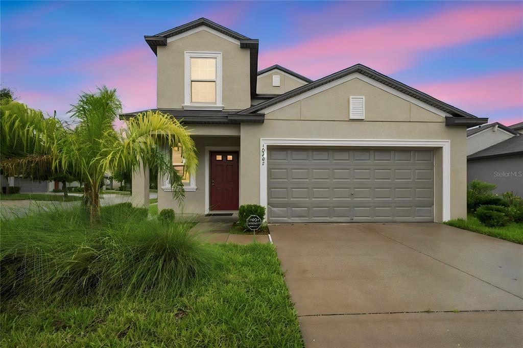 A two-story house with a beige stucco exterior, a red front door, and a two-car garage — 10202 HAPPY HEART AVENUE, RIVERVIEW, FL