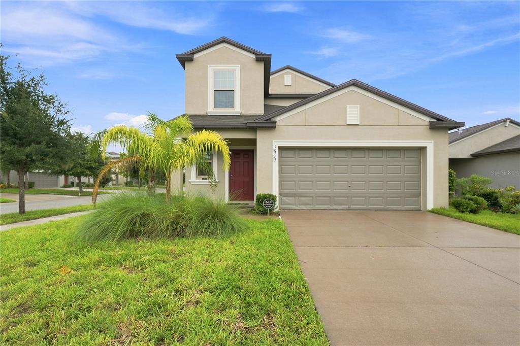 A two-story suburban house with a tan stucco exterior, a red front door, and a garage — 10202 HAPPY HEART AVENUE, RIVERVIEW, FL