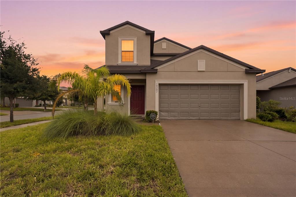 A two-story suburban house with a tan stucco exterior, a two-car garage, and a palm tree — 10202 HAPPY HEART AVENUE, RIVERVIEW, FL