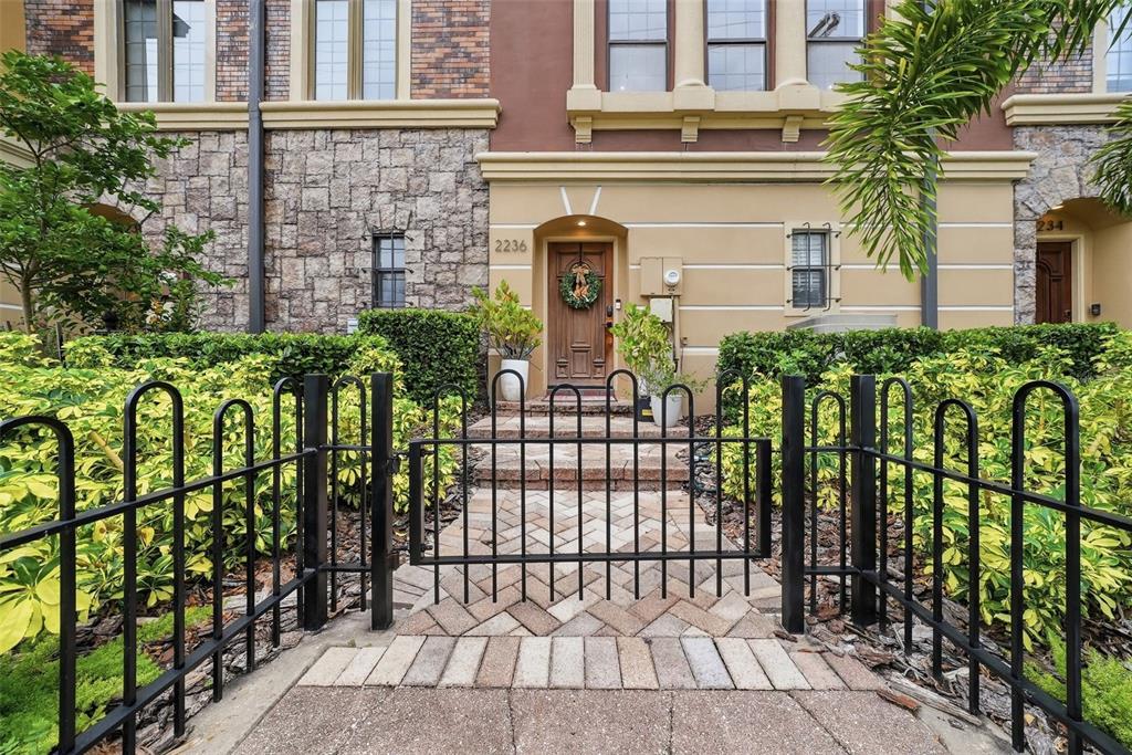 A gated brick walkway leads to the front entrance of a multi-story stone and stucco townhouse — 2236 SOHO BAY COURT, TAMPA, FL