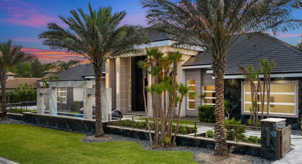 A modern luxury home exterior features a stone wall, palm trees, and a paved driveway — 420 WINGSPAN DRIVE, ORMOND BEACH, FL