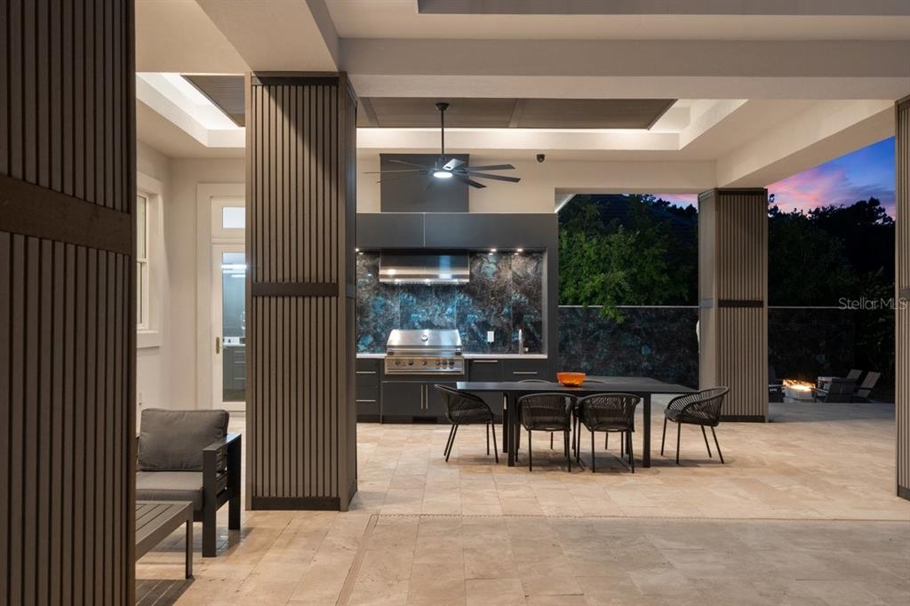 A covered outdoor patio features a built-in kitchen, dining area, and stone tile flooring — 420 WINGSPAN DRIVE, ORMOND BEACH, FL