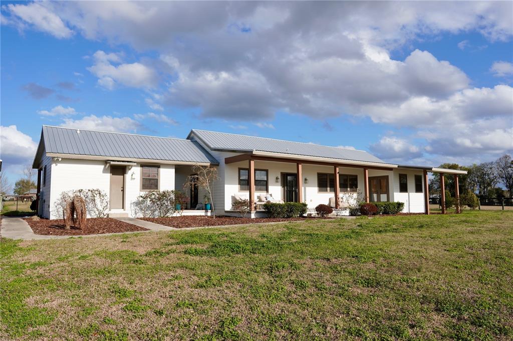 A single-story house with a metal roof and a covered porch sits on a lawn — 12895 NW GAINESVILLE ROAD, REDDICK, FL