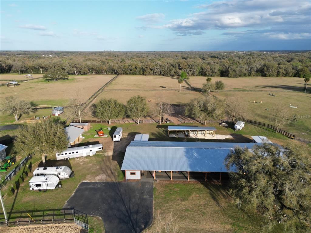 An aerial view shows a large metal-roofed barn, horse trailers, and fenced pastures — 12895 NW GAINESVILLE ROAD, REDDICK, FL