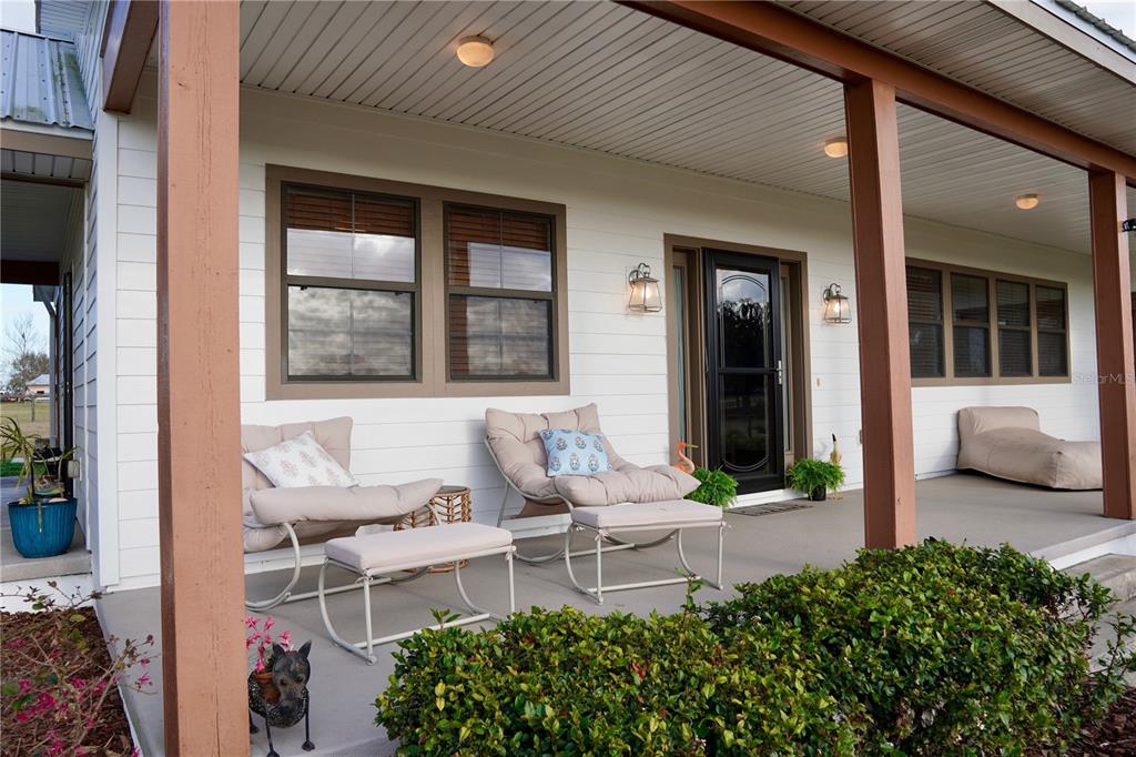 A covered front porch features white siding, brown trim, and two lounge chairs with ottomans — 12895 NW GAINESVILLE ROAD, REDDICK, FL
