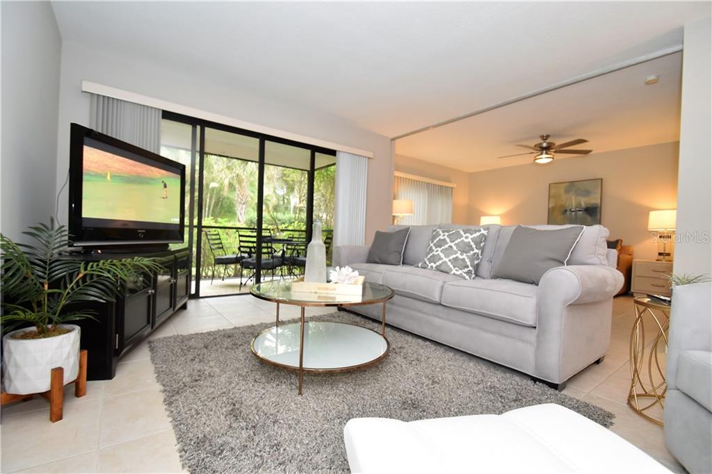 A living room features a grey sofa, a glass coffee table, and a television stand — 1667 BROOKHOUSE CIRCLE UNIT BR128, SARASOTA, FL