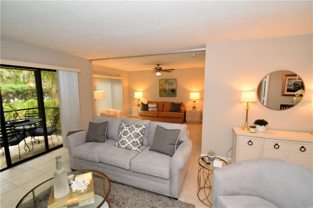 A living room with a gray sofa, a glass coffee table, and an adjacent dining area — 1667 BROOKHOUSE CIRCLE UNIT BR128, SARASOTA, FL