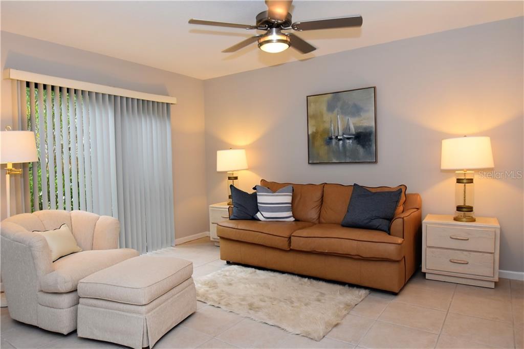 A living room features a tan leather sofa, a beige armchair with ottoman, and tile flooring — 1667 BROOKHOUSE CIRCLE UNIT BR128, SARASOTA, FL