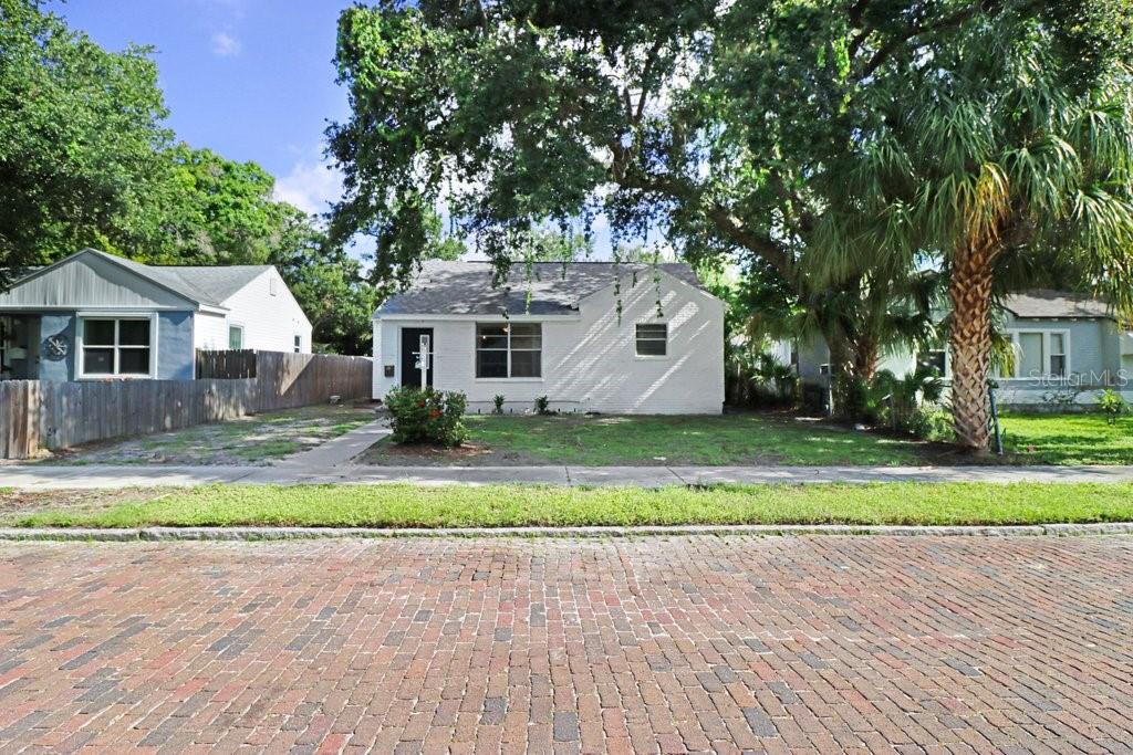 A single-story white house with a brick street in the foreground and large trees — 711 16TH AVENUE S, ST PETERSBURG, FL