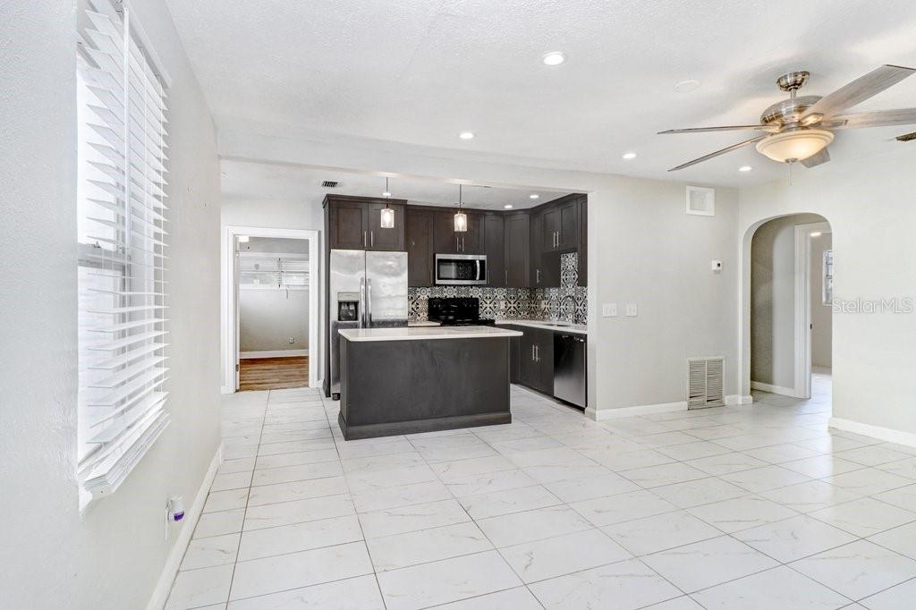 A kitchen with dark cabinets and a central island opens into a tiled living area — 711 16TH AVENUE S, ST PETERSBURG, FL