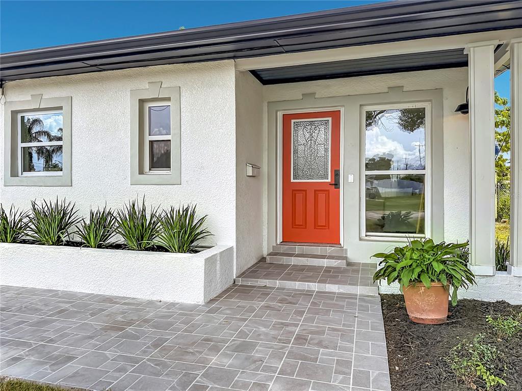 The exterior of a house features a bright orange front door and a tiled entryway — 415 MERCADO AVENUE, ORLANDO, FL