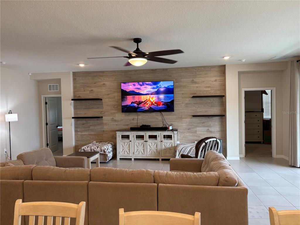 A living room features a wood-paneled accent wall with a mounted television and floating shelves — 5870 SW 80TH PLACE, OCALA, FL