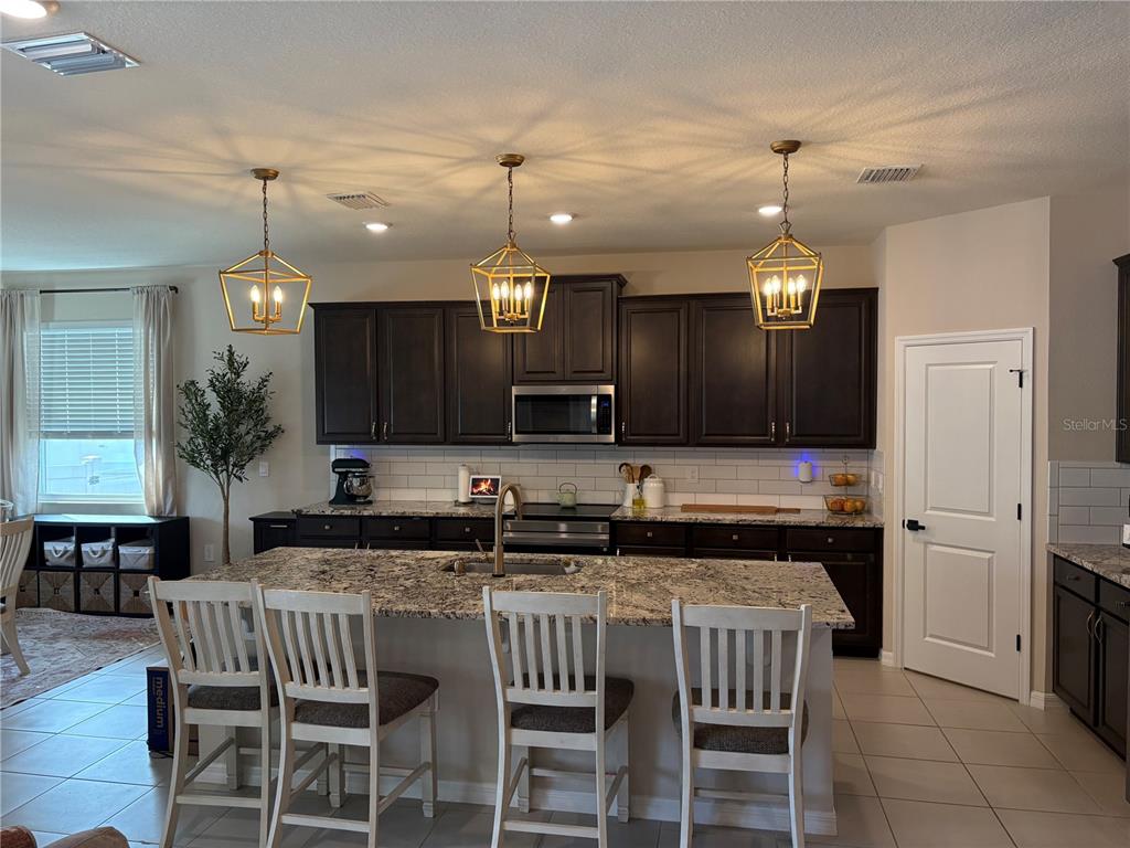 A kitchen features dark wood cabinets, granite countertops, a central island, and three pendant lights — 5870 SW 80TH PLACE, OCALA, FL