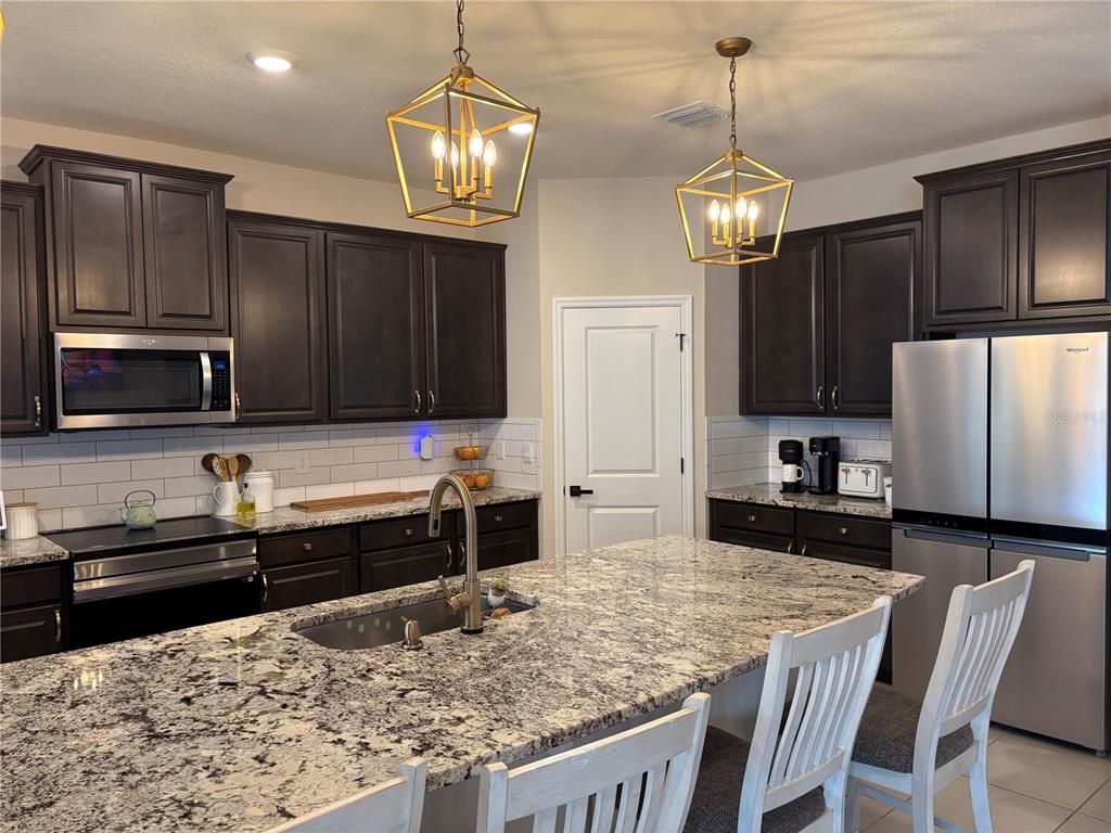A kitchen features dark wood cabinets, granite countertops, a central island, and two pendant lights — 5870 SW 80TH PLACE, OCALA, FL