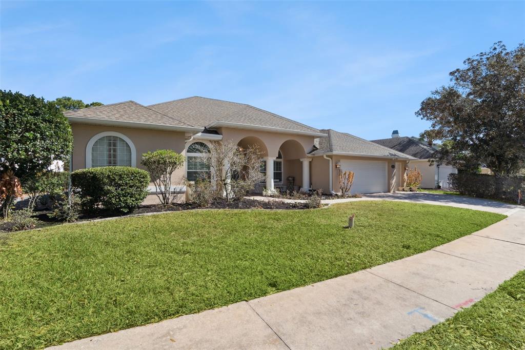 A beige house exterior features arched entryways, white columns, and a garden with blooming flowers — 1500 EDGEWATER DRIVE, MOUNT DORA, FL